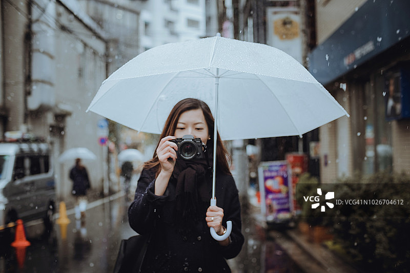 日本东京，一名女性游客在下雪时拿着雨伞通过相机拍照图片素材