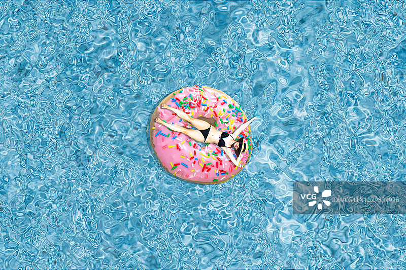在游泳池里漂浮在粉色甜甜圈甜点上的女人。图片素材
