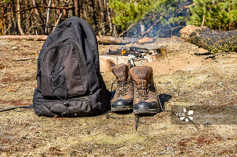 背包和旅游靴在一个针叶林的地面上。篝火的背景图片素材