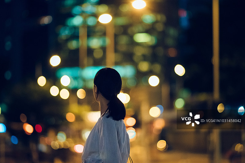 年轻女子的后视图望向照亮的城市天际线在晚上图片素材