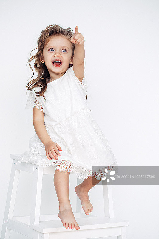 穿着白色连衣裙的可爱小女孩对着镜头微笑图片素材