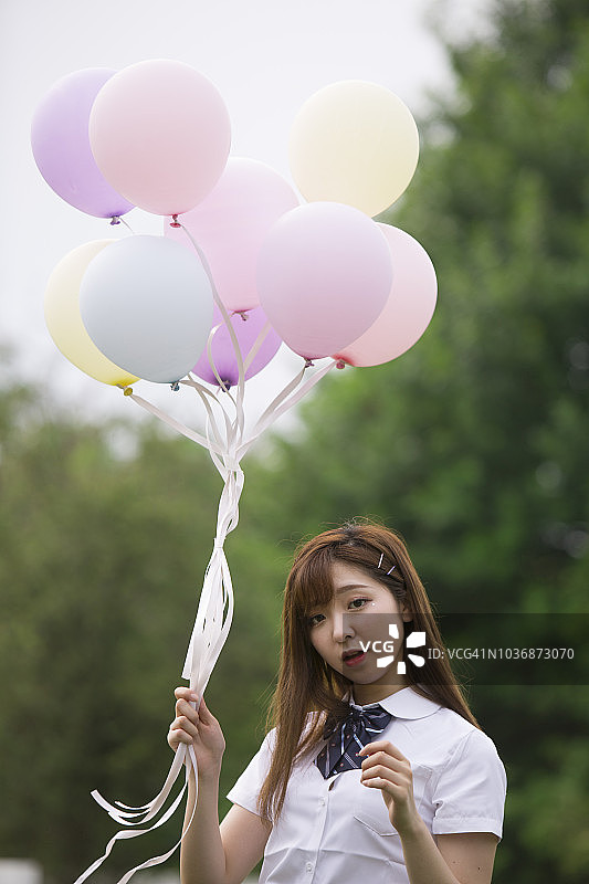 年轻美丽的女孩在公园的草地上拿着彩色的气球。图片素材