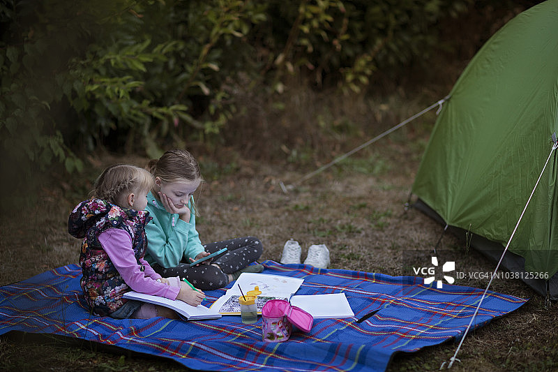 两个孩子坐在野炊地毯上，手里拿着艺术产品和智能手机图片素材