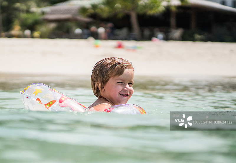 快乐的小男孩享受在充气环在海上游泳。图片素材