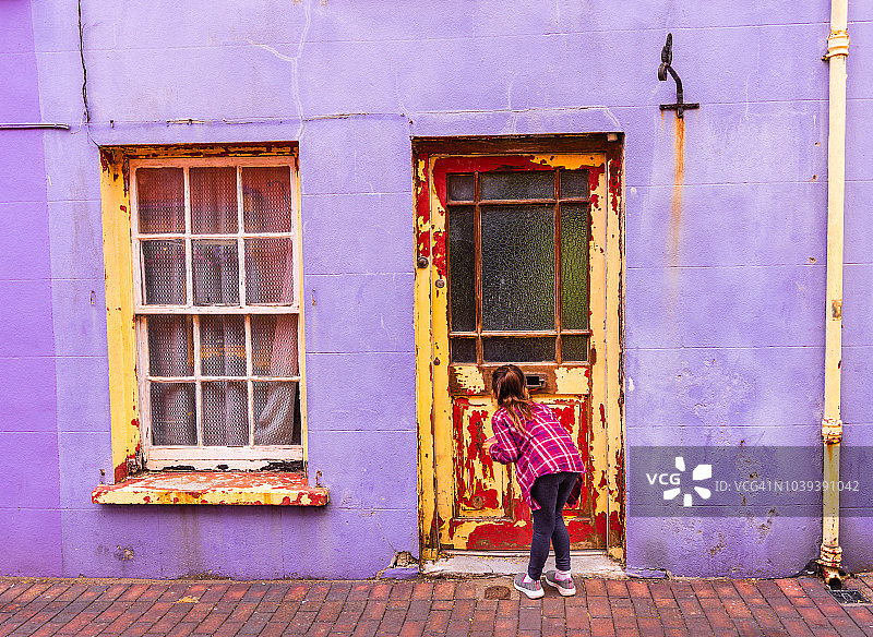 爱尔兰金赛尔，一个小女孩正在从一扇风化的门的邮件槽里看图片素材