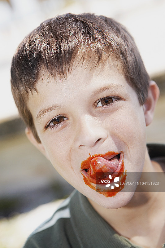 一个男孩舔着嘴唇上的番茄酱的画像图片素材