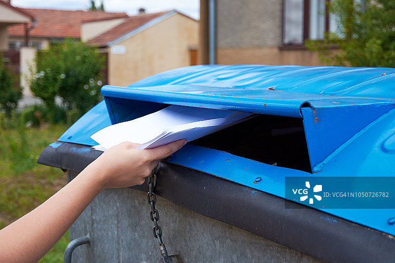 一名年轻女子把纸质文件扔进一个蓝色的容器里，用来装分类后的垃圾图片素材