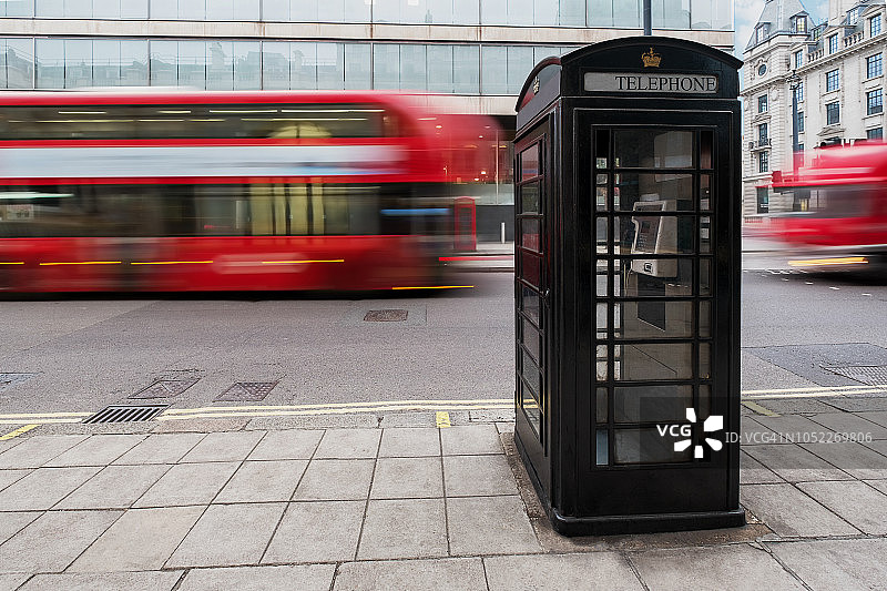 一辆标志性的红色伦敦巴士经过一个标志性的伦敦电话亭图片素材