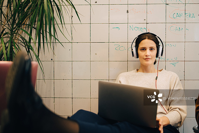 自信的年轻女性电脑黑客的肖像，通过耳机听，而坐在笔记本电脑对瓷砖w图片素材