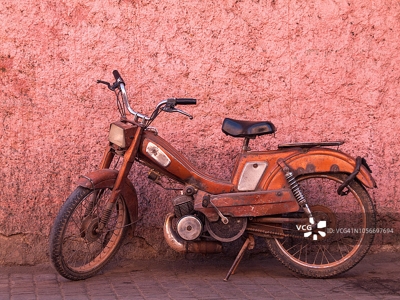 摩洛哥马拉喀什，一辆橙色的旧摩托车停在粉红色的墙前图片素材