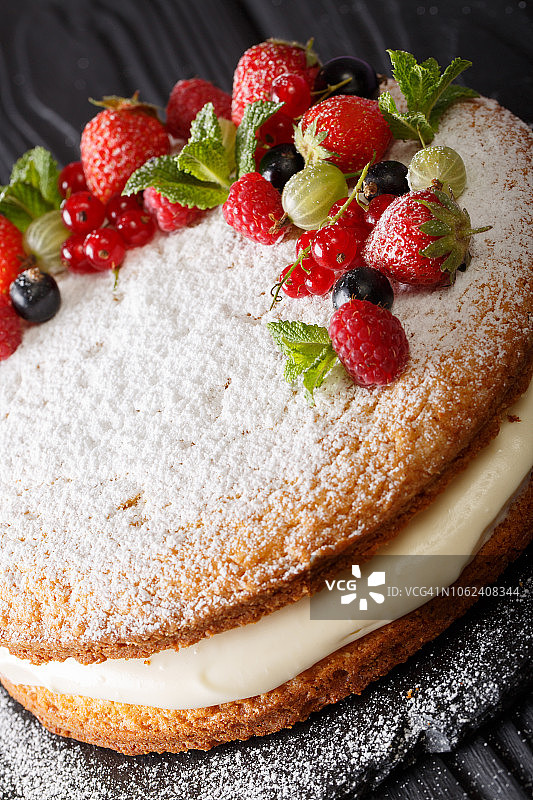 美味的维多利亚三明治蛋糕与新鲜的夏季浆果和薄荷特写。垂直图片素材
