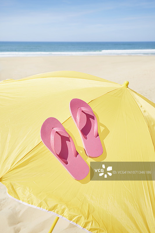 夏日的乐趣，一双粉红色的人字拖躺在沙滩和海边的黄色阳伞上图片素材