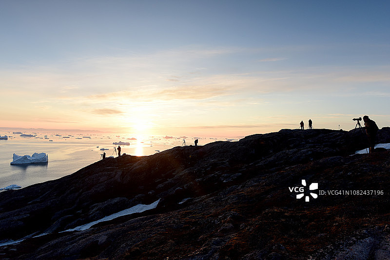 格陵兰的北冰洋上，人们在日落时在山顶上剪影图片素材