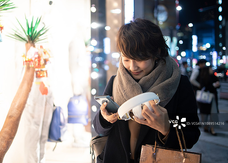 一名年轻女子在圣诞夜手持智能手机和耳机图片素材