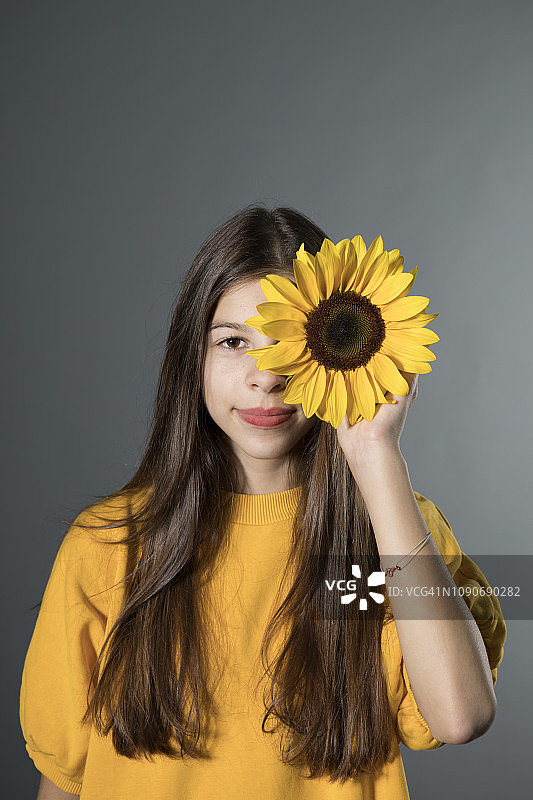 微笑的女孩与向日葵在灰色的背景前肖像图片素材