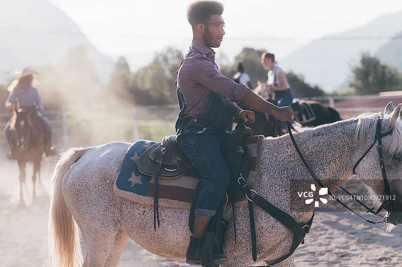 年轻男子和朋友在乡村马术竞技场骑马，Primaluna，特伦蒂诺-上阿迪杰，意大利图片素材