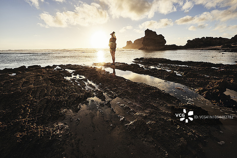 夕阳西下时，一个女人站在海岸线上图片素材