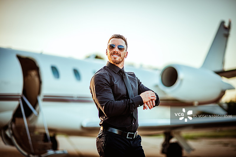 富有而成功的年轻商人在一架私人飞机前看他的手表图片素材