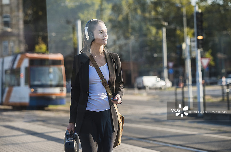 年轻女子戴着耳机和手机在电车站图片素材