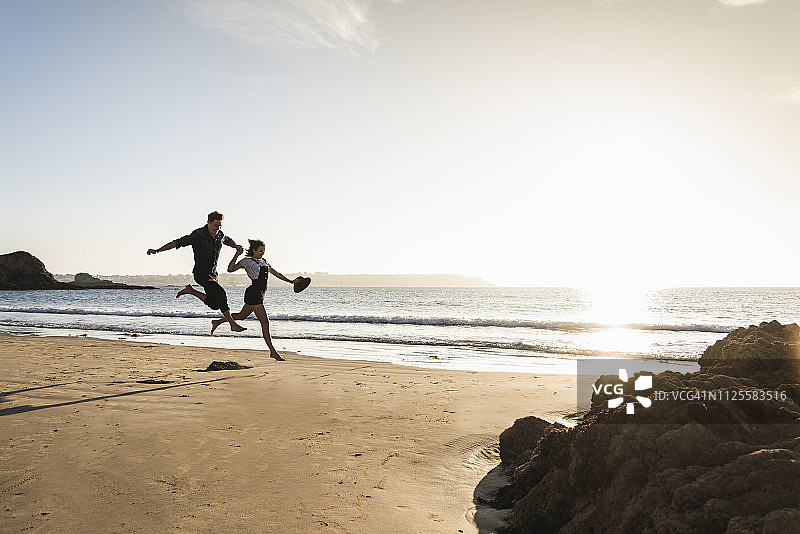 法国，布列塔尼，幸福的年轻夫妇在日落的海滩上跳跃图片素材