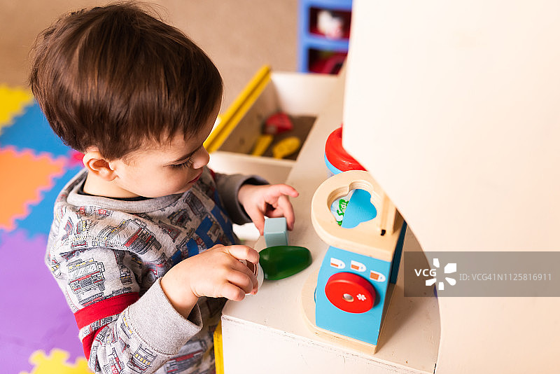 蹒跚学步的孩子玩复古厨房在玩垫与玩食物和用具。冲破主题。他正在玩一个咖啡壶。图片素材
