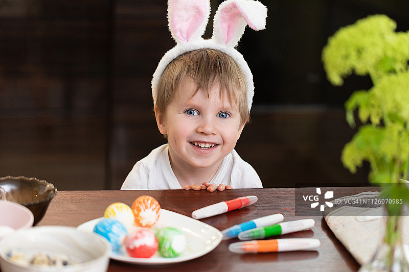 可爱的小男孩戴着复活节兔子耳朵画复活节彩蛋。图片素材