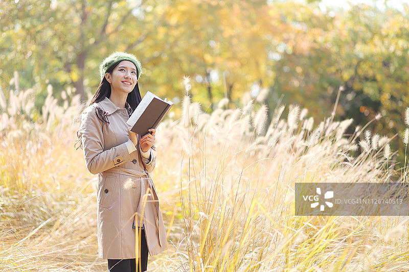 年轻女子与书站在秋天的公园图片素材