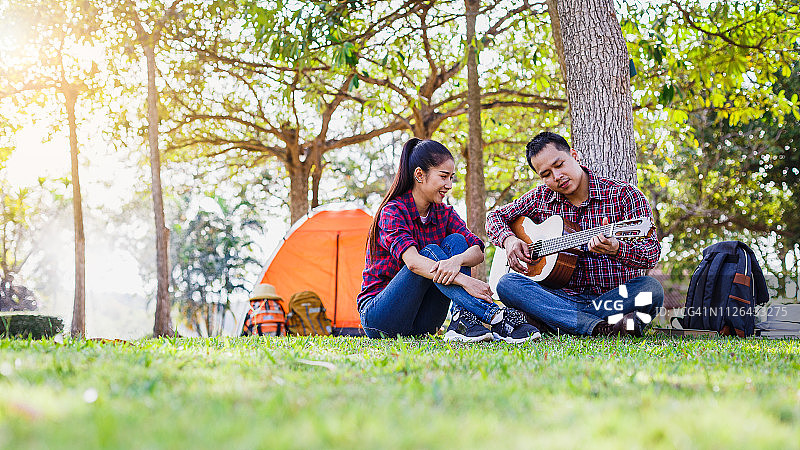 年轻的夫妇露营享受弹吉他和坐在户外露营帐篷，夫妇露营的概念图片素材