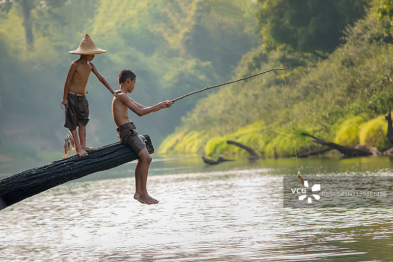 亚洲的孩子们在河边钓鱼。图片素材