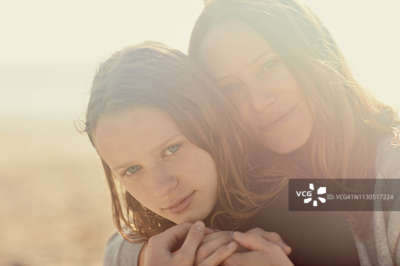 一张母亲和女儿在海滩上看着照相机的肖像图片素材