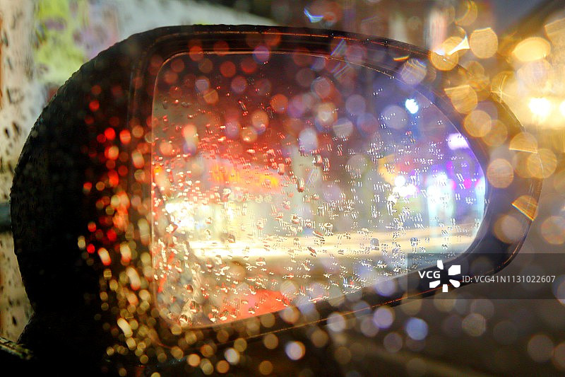 雨滴在窗户玻璃和汽车后视镜与散焦彩色灯光在背景图片素材