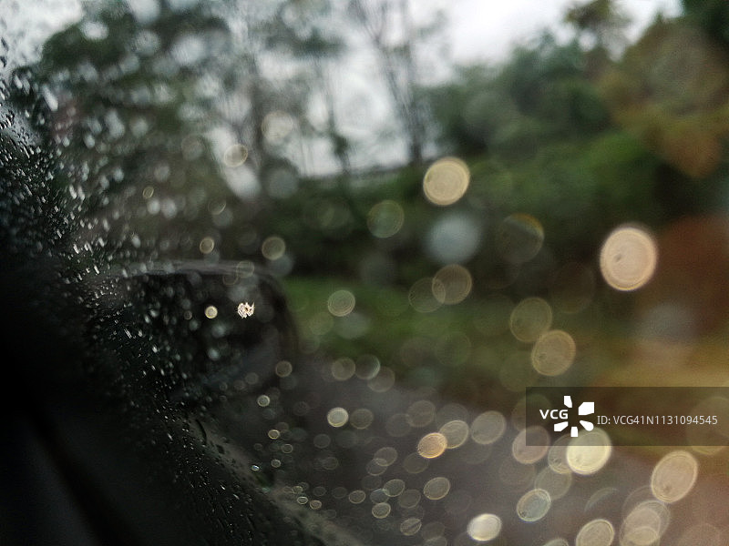 模糊的形象，雨点落在汽车车窗上与道路在雨季抽象的背景，水滴落在玻璃上，夜间暴雨下雨的汽车行驶概念。图片素材