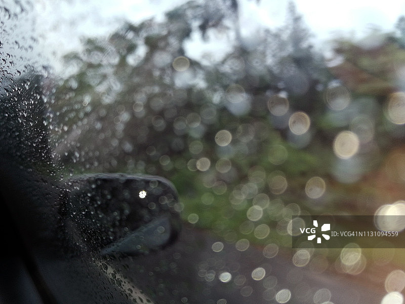 模糊的形象，雨点落在汽车车窗上与道路在雨季抽象的背景，水滴落在玻璃上，夜间暴雨下雨的汽车行驶概念。图片素材