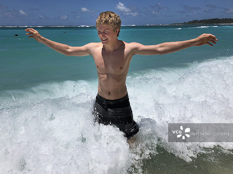 一个十几岁的男孩在海滩上笑着，玩着，享受着海水和海浪图片素材