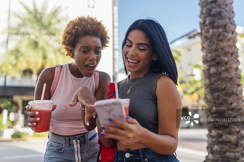美国佛罗里达州迈阿密海滩，两个快乐的女性朋友带着手机和软饮料在城市里图片素材