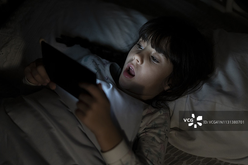 震惊的女孩晚上躺在床上玩手机图片素材
