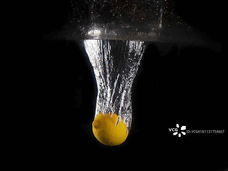 黄色柠檬落入溅起水花的黑色背景图片素材