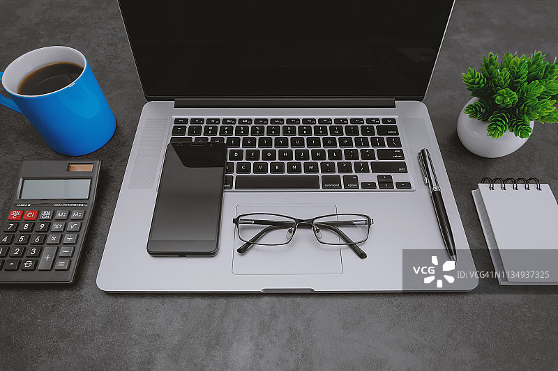 笔记本电脑，手机和蓝色咖啡杯在办公桌上图片素材
