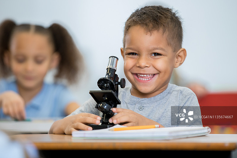 一个快乐的小男孩在STEM小学教室里使用显微镜时微笑图片素材