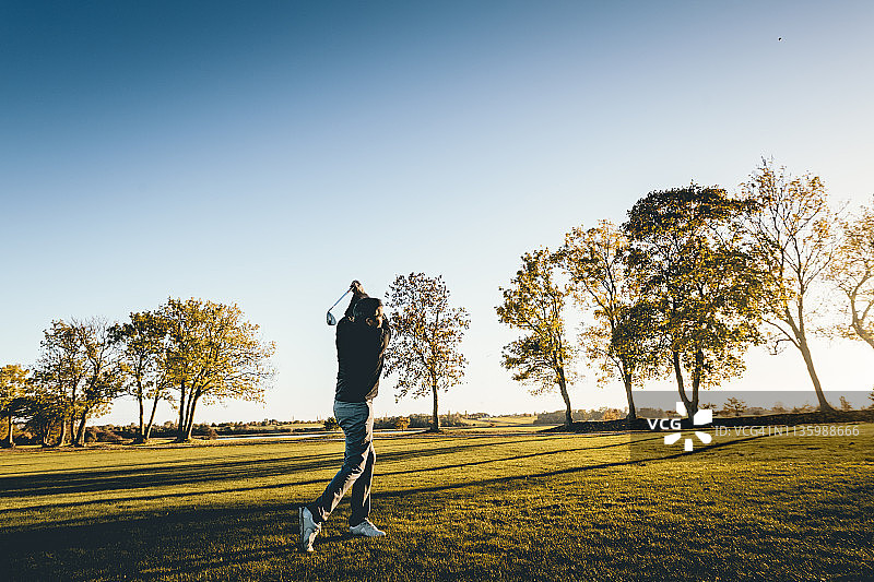 在黄昏的光线下，高尔夫球手在球道上。图片素材