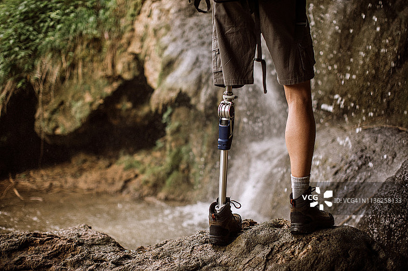 一个戴着假腿的人站在瀑布旁边的岩石上图片素材