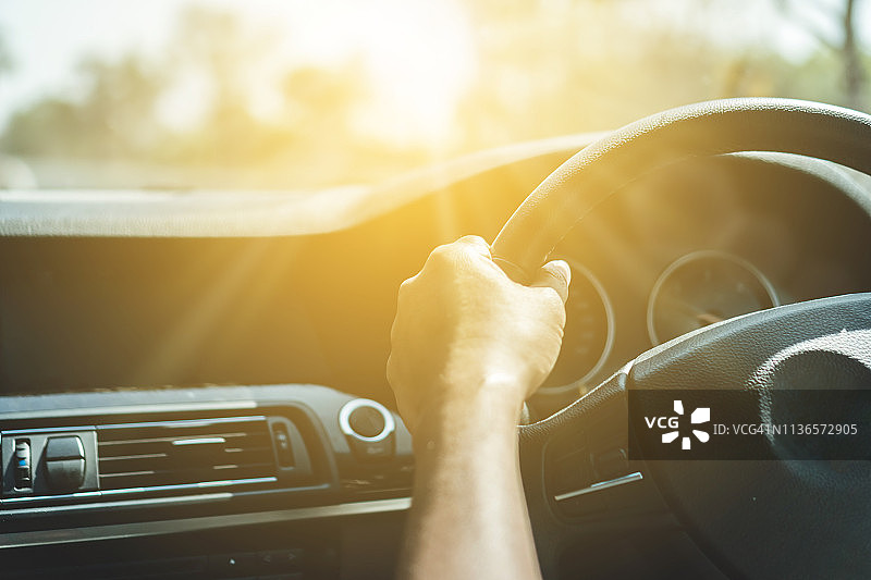 方向盘上的人的手在阳光的背景下驾驶汽车。图片素材