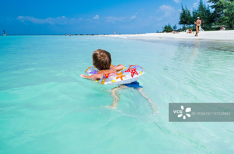 后视图的小男孩游泳与充气环在海上。图片素材
