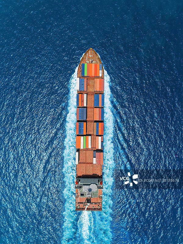 航拍俯视图集装箱船以美丽的波浪图案全速驰骋在湛蓝的大海上，从事物流、进出口、航运或运输。图片素材