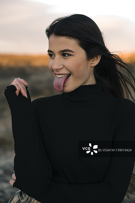 一个穿着黑色套头衫伸出舌头的少女的肖像图片素材