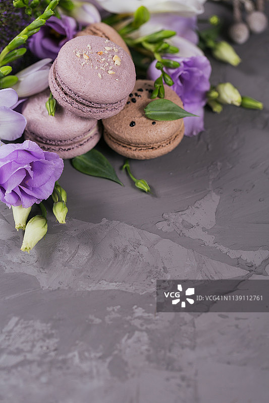 灰色的混凝土背景上是一堆甜蜜的法国马卡龙和花朵。图片素材