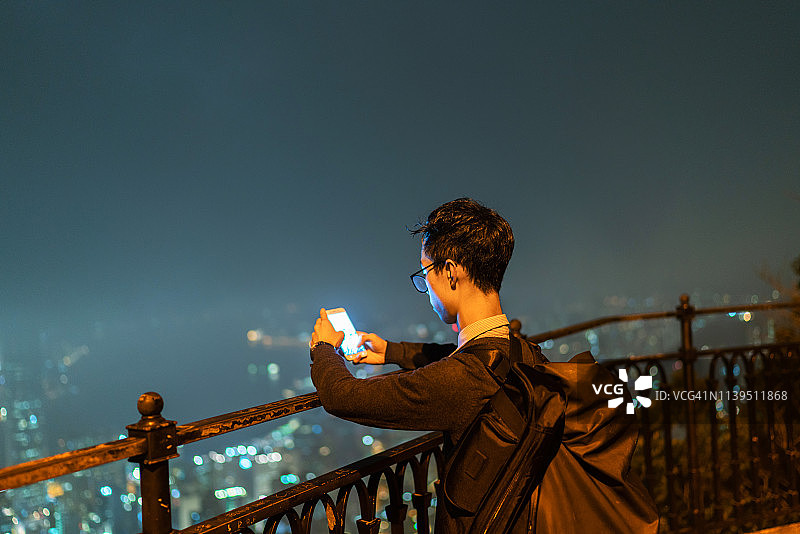 一个中国男人在晚上用手机和电脑工作图片素材