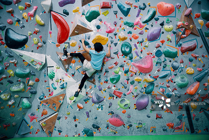 一个十几岁的女孩在攀岩馆爬着一堵抱石墙图片素材