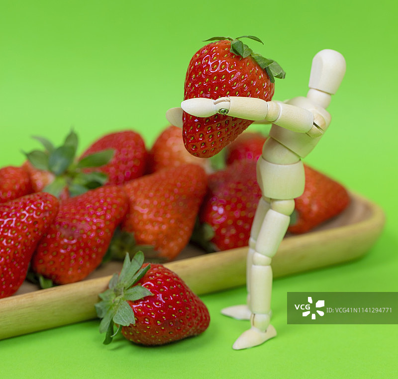 拿着水果的木制人体模型。草莓图片素材