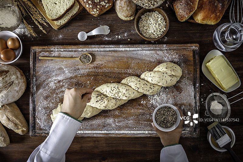 女厨师用手为面包制作香料。在一个质朴的厨房里，食材和用具围绕着切菜板框架。图片素材